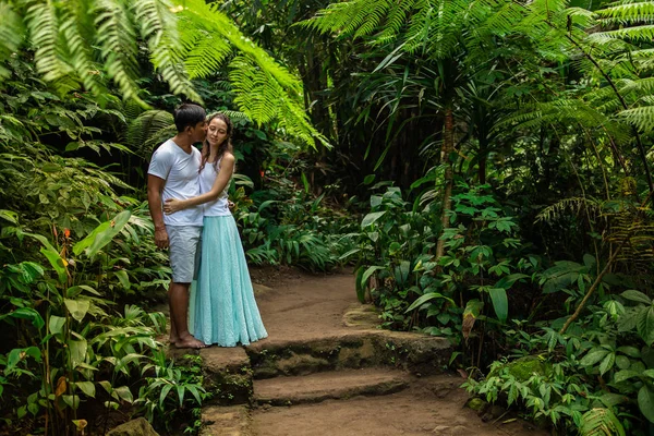 Happy цілуватися мультирасова пара обійматися на ходьбі слід в тропічному лісі. Молоді змішані гонки пара на відпочинку в Азії. Убуд, Індонезія. — стокове фото