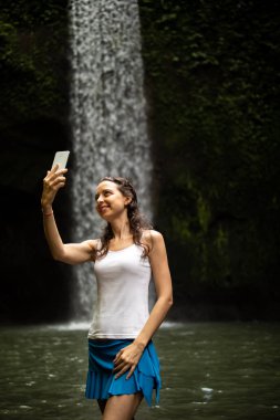 Mutlu Kafkas kadın şelale manzara zevk, şelale yakınında akıllı telefon ile selfie alarak.