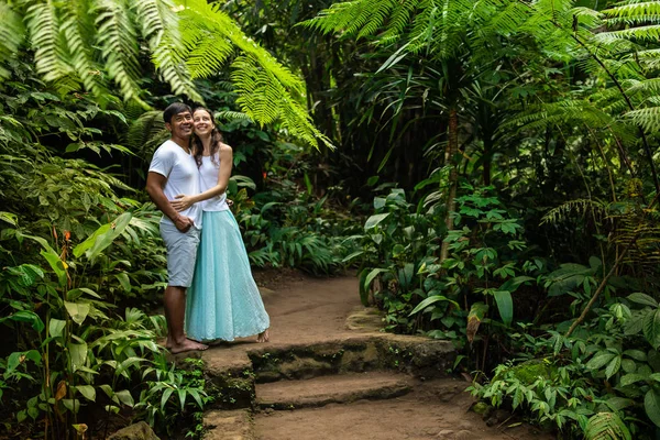 Feliz casal multirracial sorridente abraçando na trilha de caminhada na floresta tropical. Jovem casal misto em férias na Ásia. Ubud, Bali, Indonésia . — Fotografia de Stock