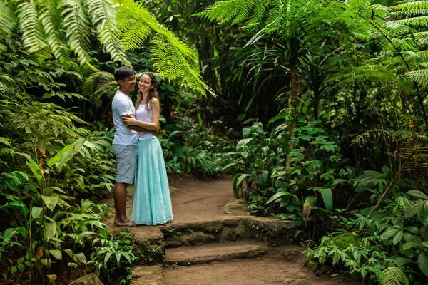 Щасливий усміхнений численне подружжя обійматися на прогулянкові стежки в тропічному лісі. Молоді змішані гонки пара на відпочинку в Азії. Убуд, Індонезія. — стокове фото
