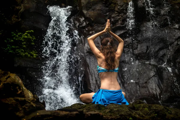 Young Caucasian woman meditating, practicing yoga at waterfall in Ubud, Bali, Indonesia. View from back. — Stock Photo, Image