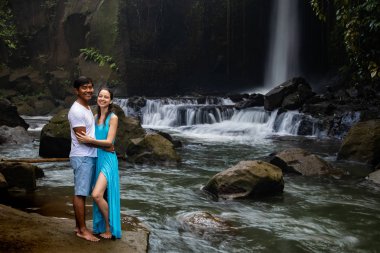 Mutlu gülümseyen çok ırklı çift tropikal ormanda şelale yakınında sarılma. Asya'da tatilde genç karışık ırk çift. Ubud, Bali, Endonezya.