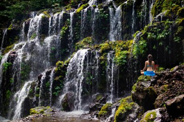 Genç Beyaz kadın meditasyon yapıyor, şelalede yoga yapıyor. Arkadan bak. Banyu Wana Amertha şelale Wanagiri, Bali, Endonezya. 