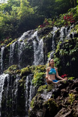 Genç Beyaz kadın meditasyon yapıyor, şelalede yoga yapıyor. Banyu Wana Amertha şelale Wanagiri, Bali, Endonezya. 