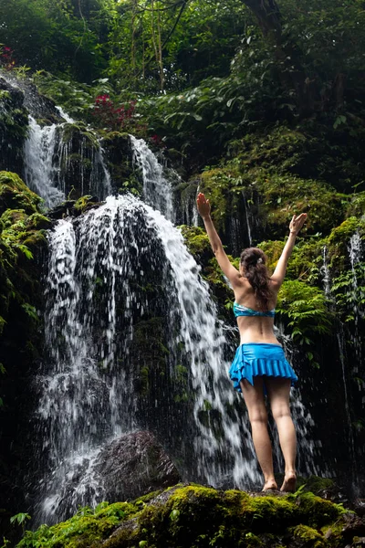 Excited Caucasian woman raising arms in front of waterfall. View from back. Banyu Wana Amertha waterfall Wanagiri, Bali, Indonesia. — Stock Photo, Image