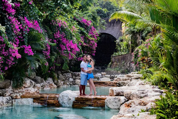 Счастливая пара в отпуске. Многонациональная пара в бассейне. Бассейн в окружении розовых бугенвиллей . — стоковое фото