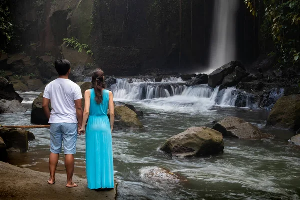 Çok ırklı çift tropikal ormanda şelale yakınında el ele tutuşuyor. Asya'da tatilde genç karışık ırk çift. Arkadan bak. Ubud, Bali, Endonezya.