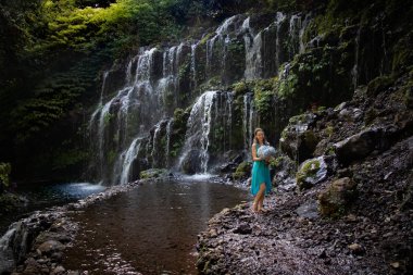 Şelalenin yanında ortanca buket tutan genç bir kadın. Güzel mavi ortanca çiçekler. Düğün öncesi photoshoot. Bali