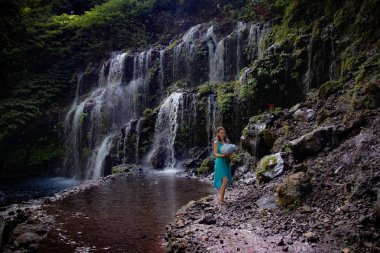 Şelalenin yanında ortanca buket tutan genç bir kadın. Güzel mavi ortanca çiçekler. Düğün öncesi photoshoot. Bali