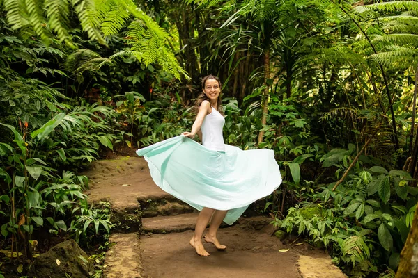 Szczęśliwa młoda kobieta tańcząca na szlaku w tropikalnym lesie. Podróże. Wycieczka do Ubud, Bali, Indonezja. — Zdjęcie stockowe