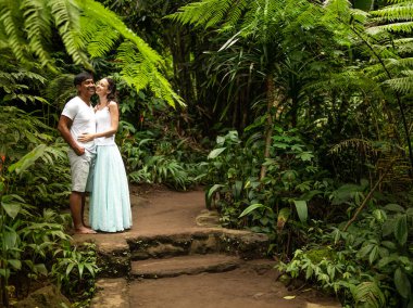 Mutlu gülümseyen çok ırklı çift tropikal ormanda yürüyüş yolunda sarılıp öpüşüyor. Asya 'da tatilde olan genç melez bir çift. Ubud, Bali, Endonezya.