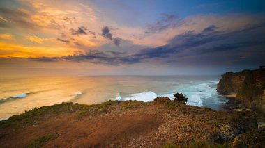 İnanılmaz bir deniz manzarası. Bali 'deki Uluwatu uçurumundan muhteşem bir manzara. Gün batımı zamanı. Mavi saat. Hareket köpüklü okyanus. Bulutlu gökyüzü. Doğa konsepti. Yumuşak odaklanma. Yavaş deklanşör hızı.