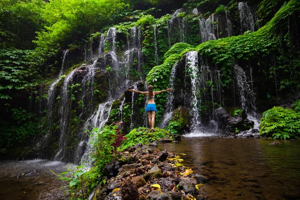 旅行生活方式 热带森林瀑布处穿着比基尼的年轻女旅行家 兴奋的女人在瀑布前举起胳膊从后面看Banyu Wana Amertha瀑布Wanagiri — 图库照片