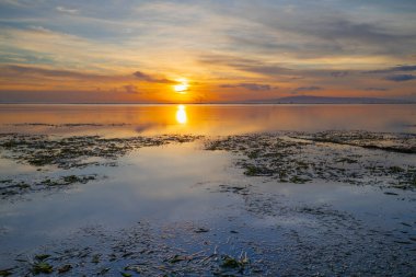 Ufukta doğan güneş. Gün doğumu deniz manzarası. İnanılmaz bir su yansıması. Bulutlu gökyüzü. Ufukta parlak güneş ışığı var. Kapama hızı yavaş. Yumuşak odaklanma. Sanur Plajı, Bali, Endonezya.