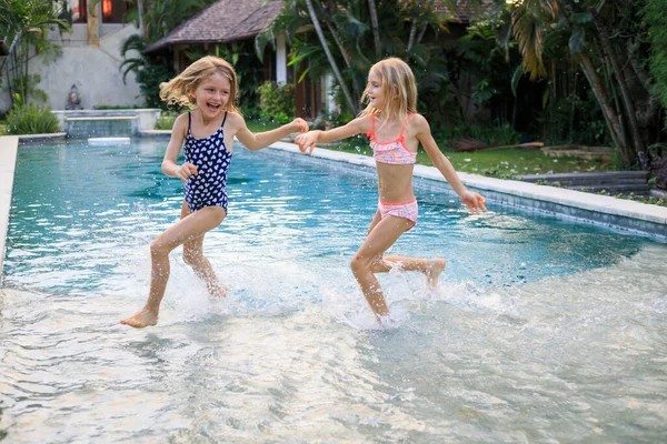 Yüzme havuzunda koşan küçük kızlar. Kız kardeşler birlikte oynuyorlar. Yaz kavramı. Aile aktiviteleri. Mutlu bir çocukluk. Asya 'da tatil. Bali, Endonezya