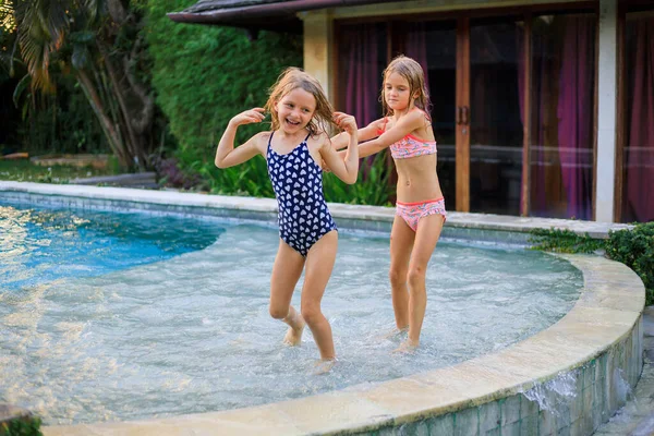 Yüzme havuzunda koşan küçük kızlar. Kız kardeşler birlikte oynuyorlar. Yaz kavramı. Aile aktiviteleri. Mutlu bir çocukluk. Asya 'da tatil. Bali, Endonezya