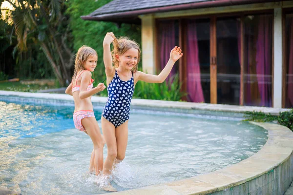 Yüzme havuzunda koşan küçük kızlar. Kız kardeşler birlikte oynuyorlar. Yaz kavramı. Aile aktiviteleri. Mutlu bir çocukluk. Asya 'da tatil. Bali, Endonezya