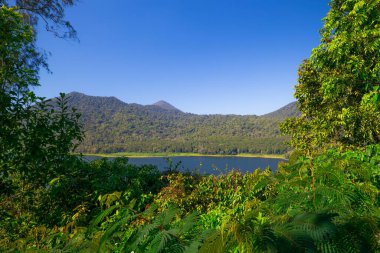 Panoramik manzara. Tepeler, dağlar ve tropikal yağmur ormanlarıyla çevrili göl manzaralı. Beyaz bulutlu mavi gökyüzü. Parlak güneş ışığı. Bedugul 'daki Buyan Gölü, Bali, Endonezya