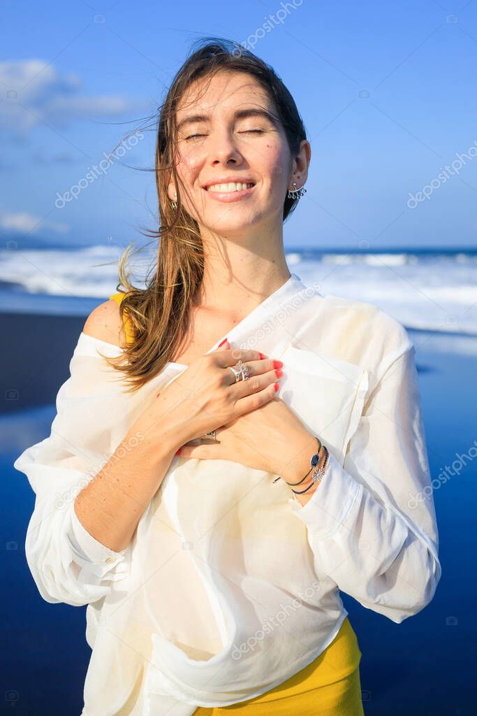 Portrait of beautiful smiling woman with jewelry. Closed eyes. Hair and clothes are blown by the wind. Happy Caucasian woman enjoying sunlight. Travel lifestyle. Bali, Indonesia