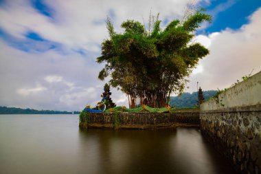 Bali adasındaki Pura Ulun Danu Bratan tapınağı. Yılan heykelleri ve bambularla dolu bir tapınak. Bali 'nin simgesi. Bulutlu gökyüzü. Su yansıması. Kapama hızı yavaş. Bratan Gölü, Bali, Endonezya