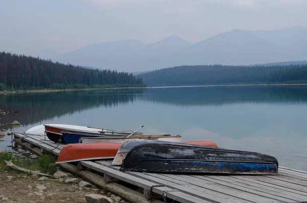 A small lake near Jasper Alberta, Canada.  Residents have chained their boats to the dock to be used at there leisure to row around the protected lake.  The mountains in the background are just visible through the haze.