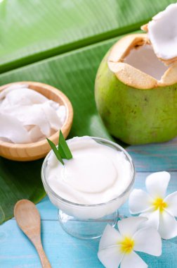 Young coconut pudding served in a glass cup decorated with coconut meat looks delicious on the banana leaves and a beautiful blue wooden table. clipart