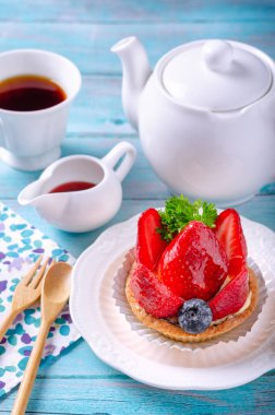 Beyaz bir tabak tabakta çilek ve yaban mersini ile dekore edilmiş meyve tart, hazır bir çay ve ahşap zemin üzerine yerleştirilen bir çaydanlık ile. Sabah atmosferi hissetmek için.