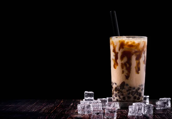 Té de leche de burbuja de hielo en vidrio en el suelo de madera. Decorado con cubitos de hielo para dar una sensación fresca. El fondo es negro . — Foto de Stock