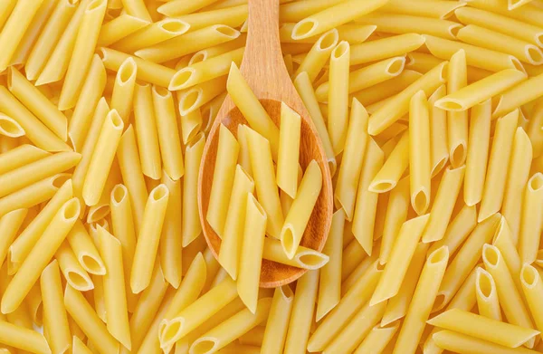 Penne rigate pasta pile background with wooden spoon. — Stock Photo, Image