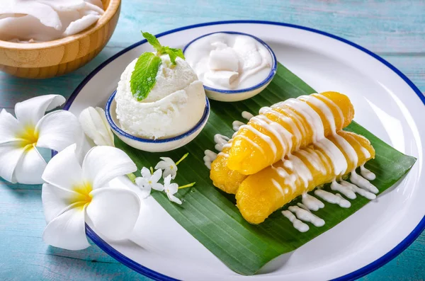 Banan w syropie zwieńczony mlekiem kokosowym, podawany z lodami z mleka kokosowego Pięknie urządzony w tradycyjnym tajskim stylu na białym talerzu. — Zdjęcie stockowe