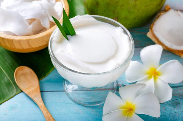 Ung kokosnöt pudding serveras i en glas kopp dekorerad med kokoskött ser läckra ut på bananbladen och en vacker blå träbord. — Stockfoto