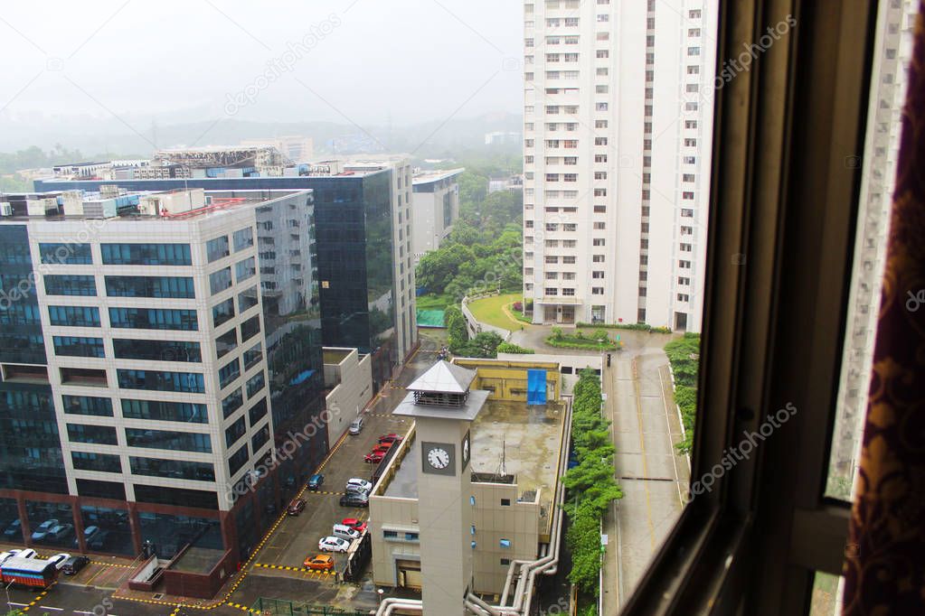 Mumbai rains through the window overlooking office buildings, apartments, roads and green hills far away