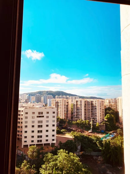 Vista de apartamentos, árvores, colinas e céu azul com nuvens parciais de uma janela em um dia ensolarado — Fotografia de Stock