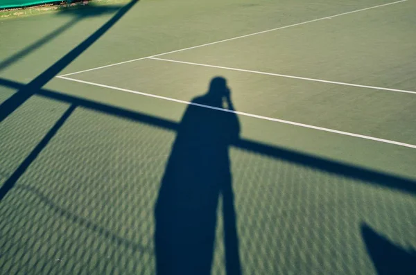 Tenis kortunda zıtlık oluşturan bir spor fotoğrafçısının gölgesi