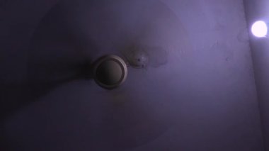 Tavan vantilatörü çatının altında asılı. Vantilatör dönüyor. Bu video çok düşük bir deklanşör hızıyla çekildi. Elektrikli vantilatör çalışıyor. Evdeki oturma odasında ışık olan tavan vantilatörü. Gece Yarısı.