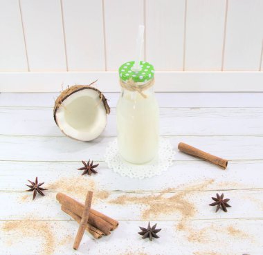 Cam bir kavanozda, beyaz arka planda hindistan cevizi kokteyli. Masada kırık hindistan cevizi var. Tarçın baharatları, yıldız anason, yemek pişirmek için..