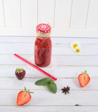 Beyaz arka planda, cam bir şişede çilek suyu. Masada çilekler var. Çilek suyu yapmak için baharatlar.