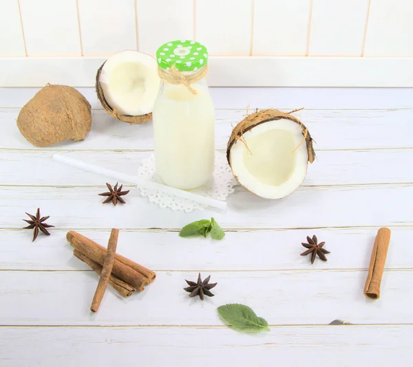 Coconut milk, in a glass bottle on a white background.Exotic fruit, coconut on the table.Spices of cinnamon, star anise and mint, for a drink.