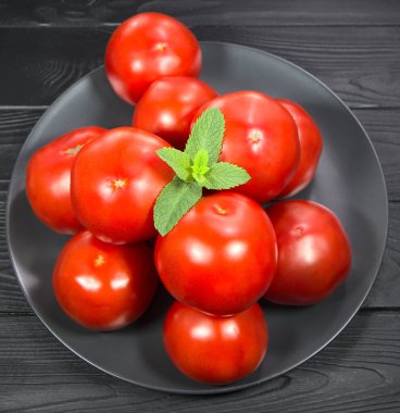 Olgun domatesler siyah bir tabakta yatıyor. Meyve suyu yapmak için sebzeler. Siyah arka planda kırmızı sebze, yemekli fotoğraf..