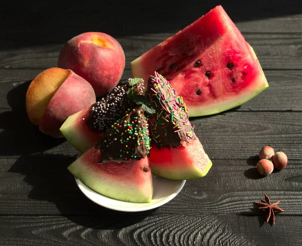 Meyveler, çikolata ve fındıklar masada. Şeftali ve karpuz, vejetaryen için vitamin seti. Tatlı ile güzel bir fotoğraf..