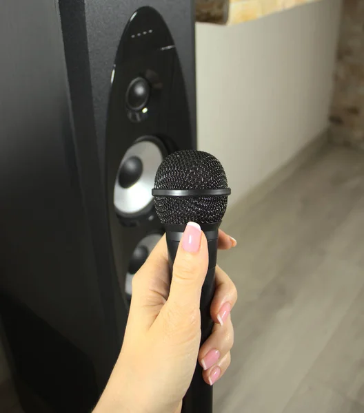 Microphone in a woman's hand, near a music speaker. Singing songs in karaoke. Interviewer holding a microphone in his hand.