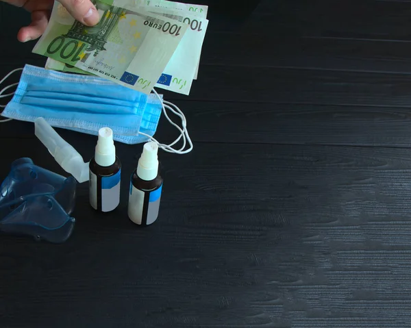 Para bir adamın elinde. Satın almak için Euro say. Spreyin maskesi ve masada antiseptik. Tıbbi maskeler, mavi, siyah bir masanın üzerinde..