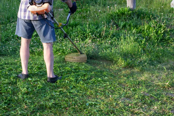 Um homem corta a relva verde com um aparador — Fotografia de Stock