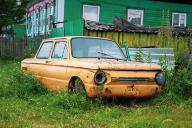 Çitin yanında terk edilmiş eski sarı bir araba duruyor. Arabanın farları yanmıyor.