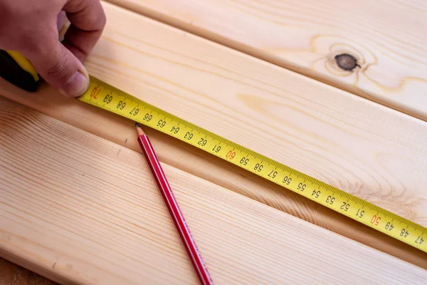 A man measures wooden boards with a tape measure and makes marks with a pencil.