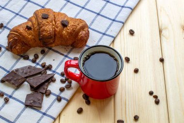 Kırmızı kahve kupası ve ahşap arka planda kruvasan. Yukarıdan gelen vize. Kahve çekirdeği ve çikolata.
