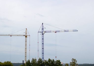 Mavi gökyüzüne karşı yüksek vinçleri olan bir inşaat alanı. Konut inşaatı devam ediyor..