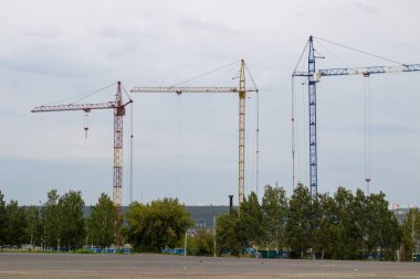 Mavi gökyüzüne karşı yüksek vinçleri olan bir inşaat alanı. Konut inşaatı devam ediyor..