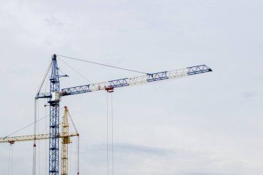 Mavi gökyüzüne karşı yüksek vinçleri olan bir inşaat alanı. Konut inşaatı devam ediyor..