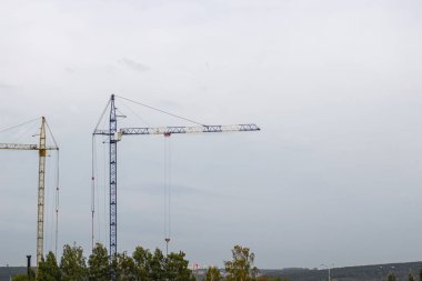 Mavi gökyüzüne karşı yüksek vinçleri olan bir inşaat alanı. Konut inşaatı devam ediyor..